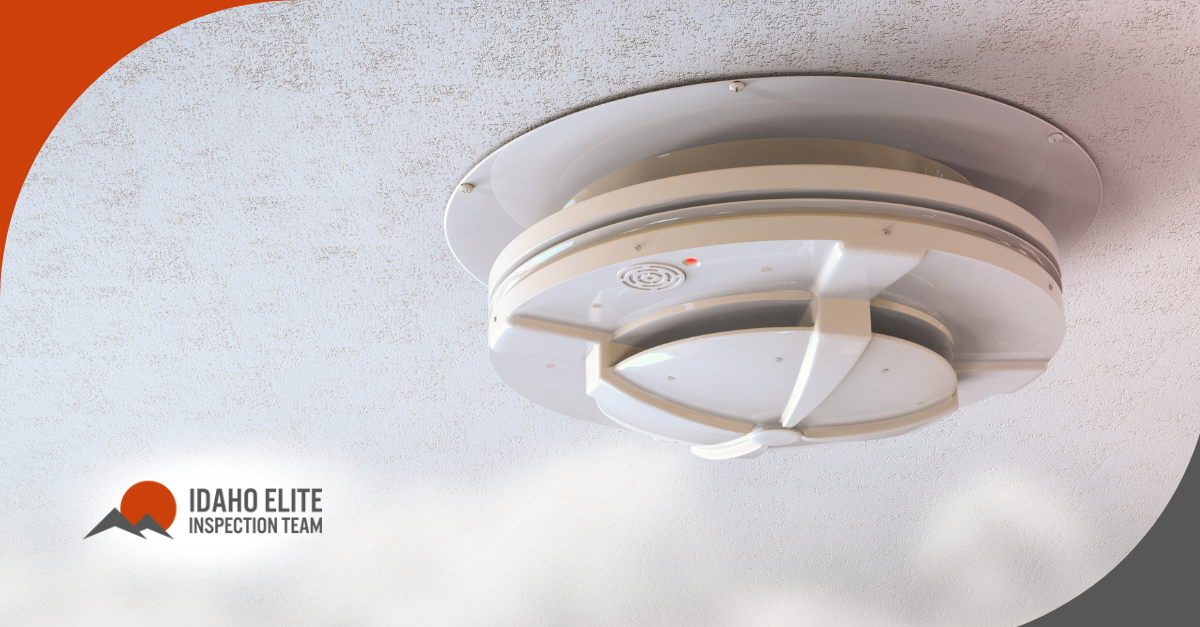 Close-up of a modern ceiling-mounted smoke detector with a red warning light