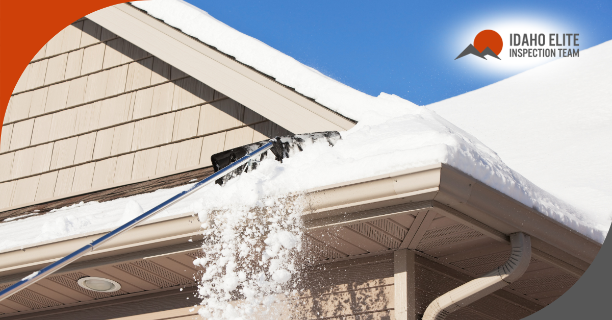 Snow being removed from a house roof with a roof rake under a clear blue sky.